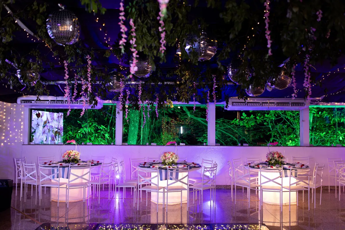 Salão com teto de flores pendentes, globos espelhados e mesas iluminadas