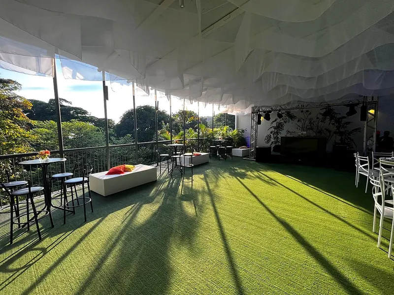 Varanda com gramado e mesas bistrô ao fim da tarde, com vista para a mata