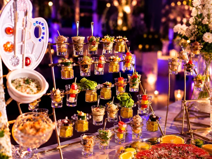 Mesa de finger food com mini porções em copinhos e espetos, montada para coquetel