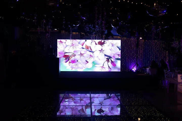 Salão escuro com painel de LED e piso iluminado exibindo flores de cerejeira