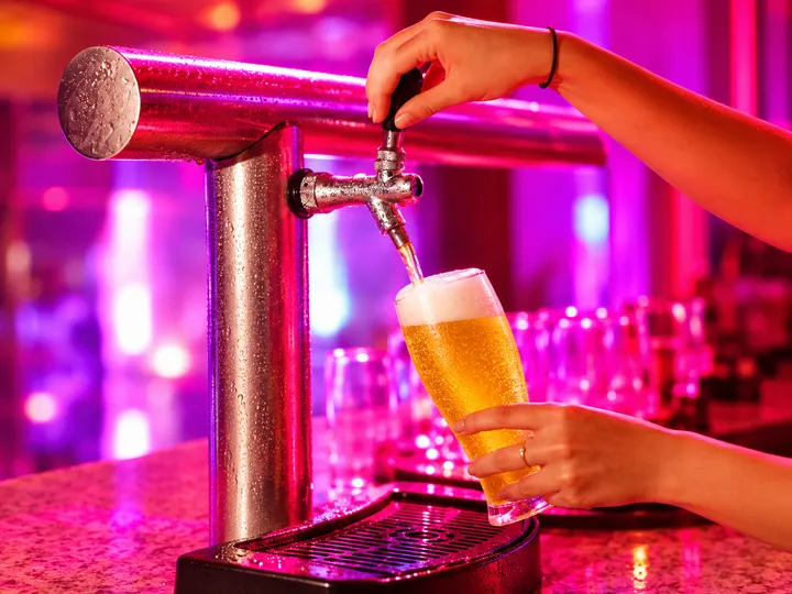 Chope sendo servido na chopeira do bar, com iluminação rosa ao fundo
